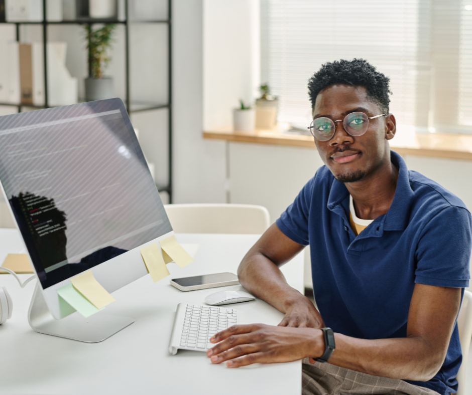 man looking at camera in front of a mac desktop computer