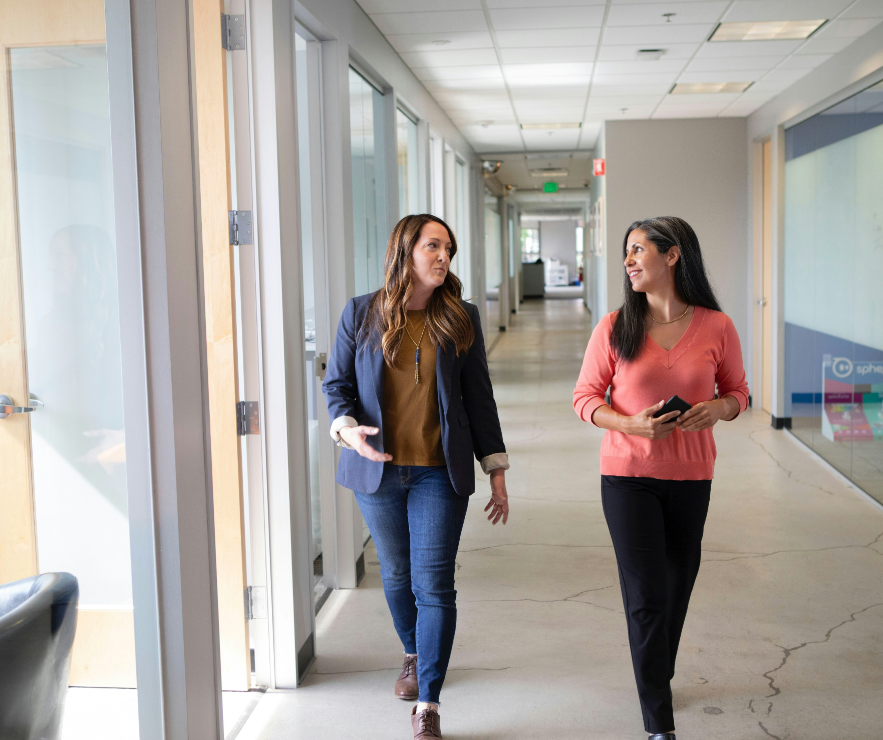 two-business-women-talking-and-walking-down-hallway